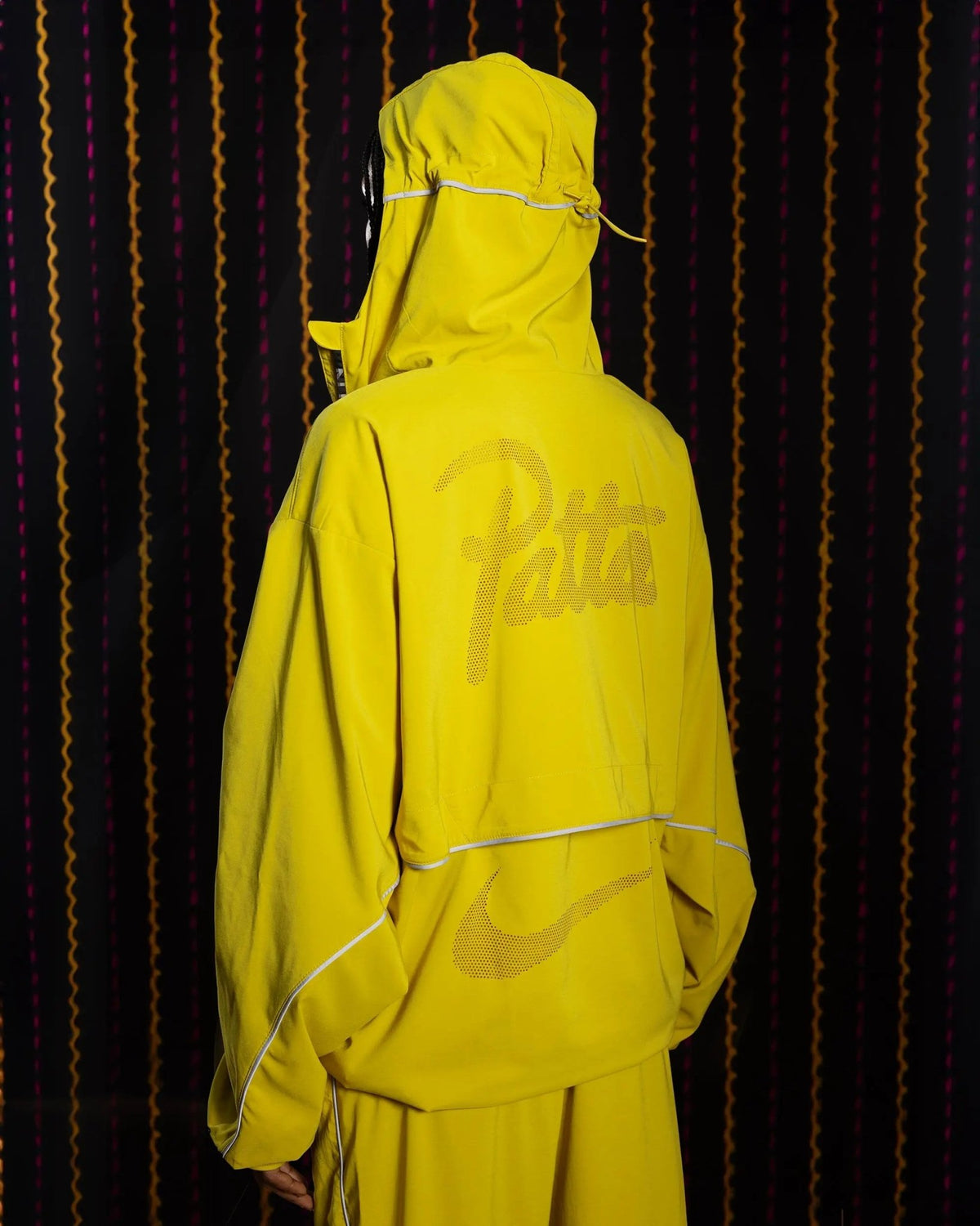 Back view of the Nike x Patta hooded track jacket in saffron quartz yellow with reflective logos.