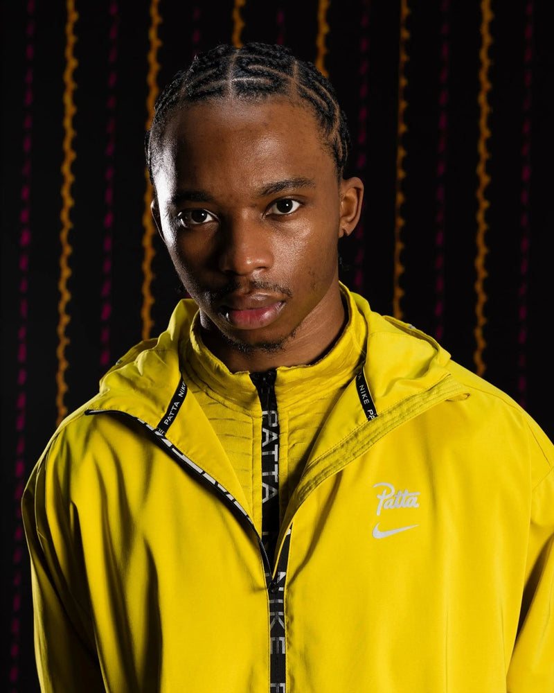 Male model wearing the yellow Nike x Patta Running Team hooded track jacket with branded zipper.