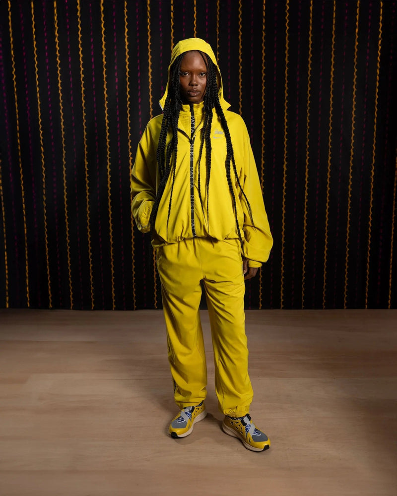 Model wearing the saffron quartz Nike x Patta Running Team hooded track jacket and matching pants.