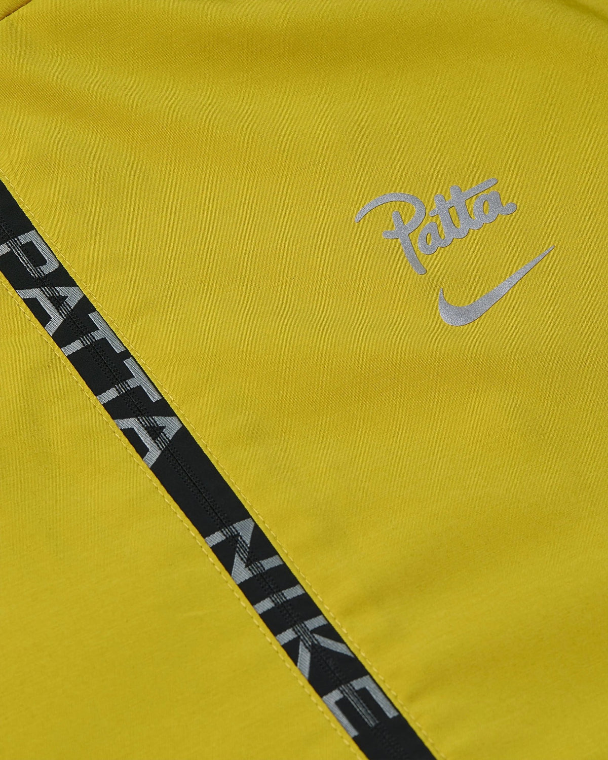 Close-up of the saffron yellow Nike x Patta track jacket with reflective logos and branded zipper.