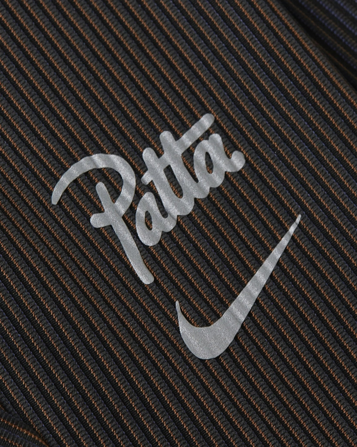 Close-up of the reflective Nike x Patta logo on black ribbed leggings.