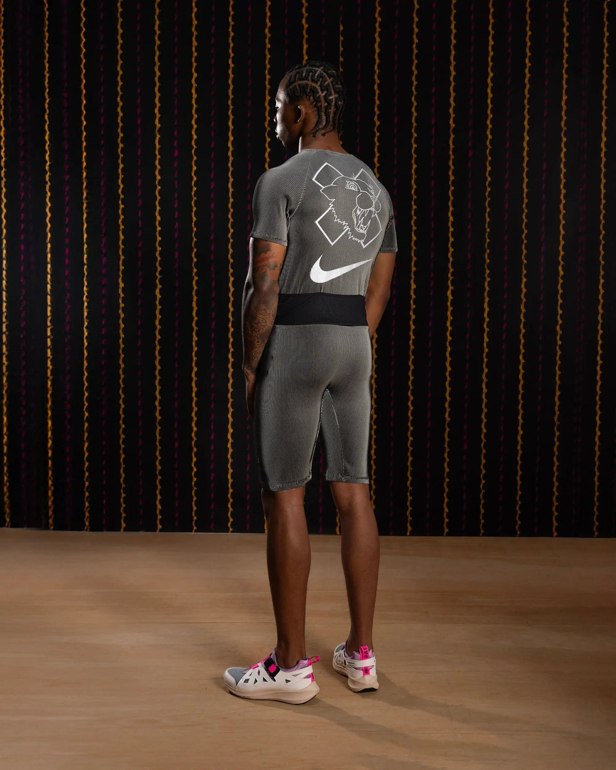 Back view of a model wearing the Nike x Patta Running Team Race Suit in black and grey with printed graphics.