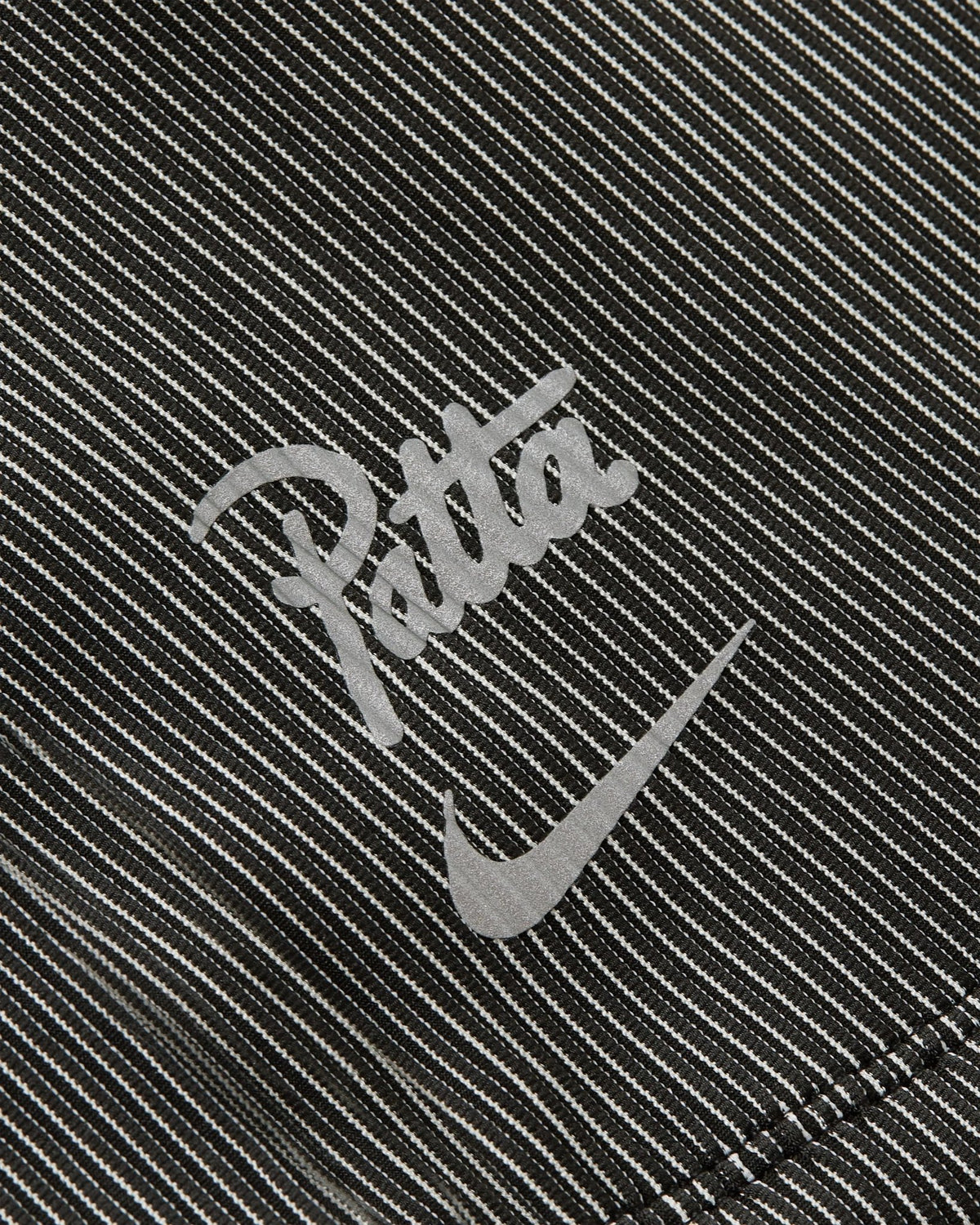 Close-up of the reflective Nike and Patta logos on the black and grey textured Running Team race suit.