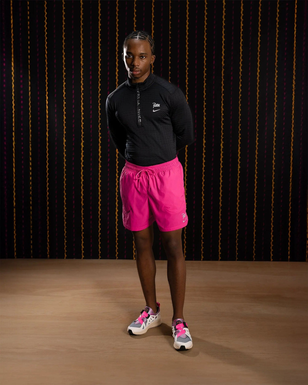 Nike x Patta Running Team shorts in fireberry pink worn by a model with a black long-sleeve top.