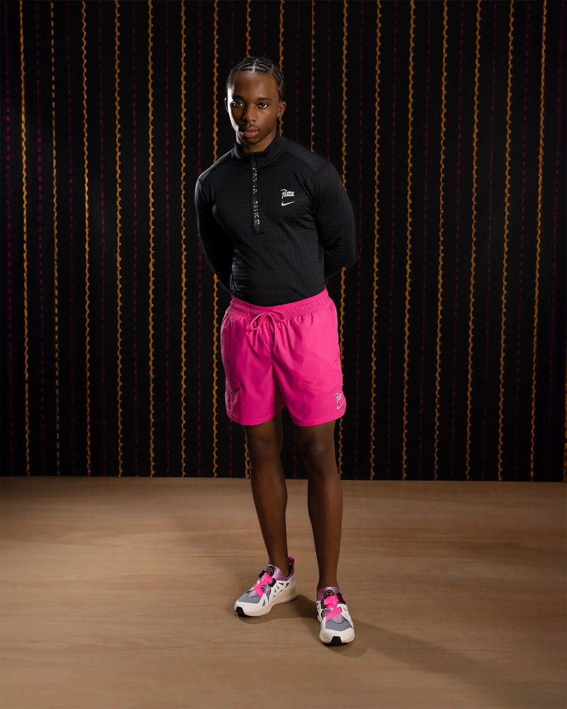 Nike x Patta Running Team shorts in fireberry pink worn by a model with a black long-sleeve top.