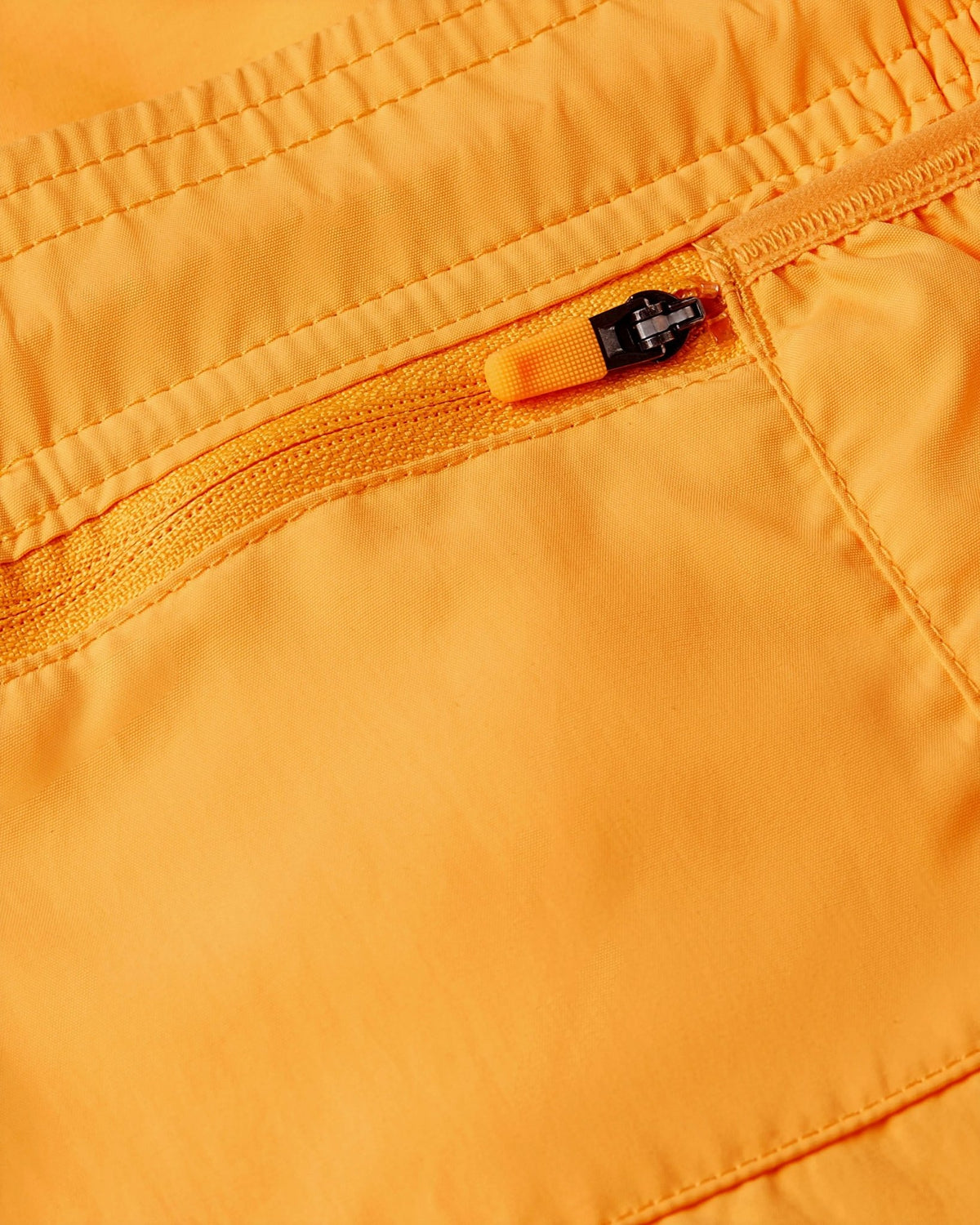 Close-up of the zippered pocket on the Nike x Patta Running Team Shorts in Sundial orange nylon.