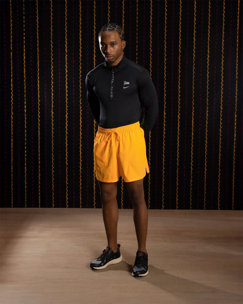 Male model wearing Sundial orange Nike x Patta Running Team shorts and a black long-sleeve top.