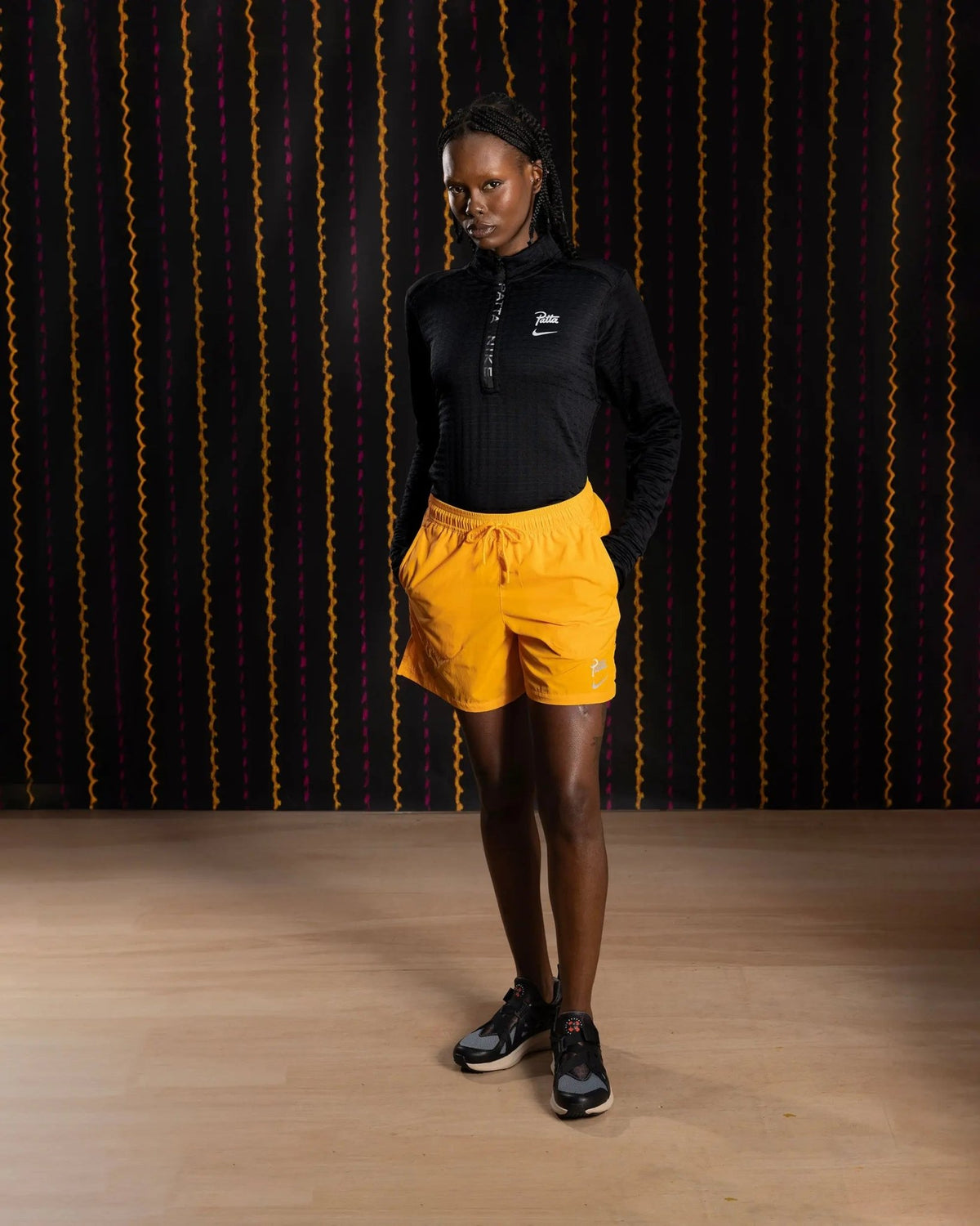 Female model wearing Nike x Patta Running Team shorts in Sundial yellow with a black top.