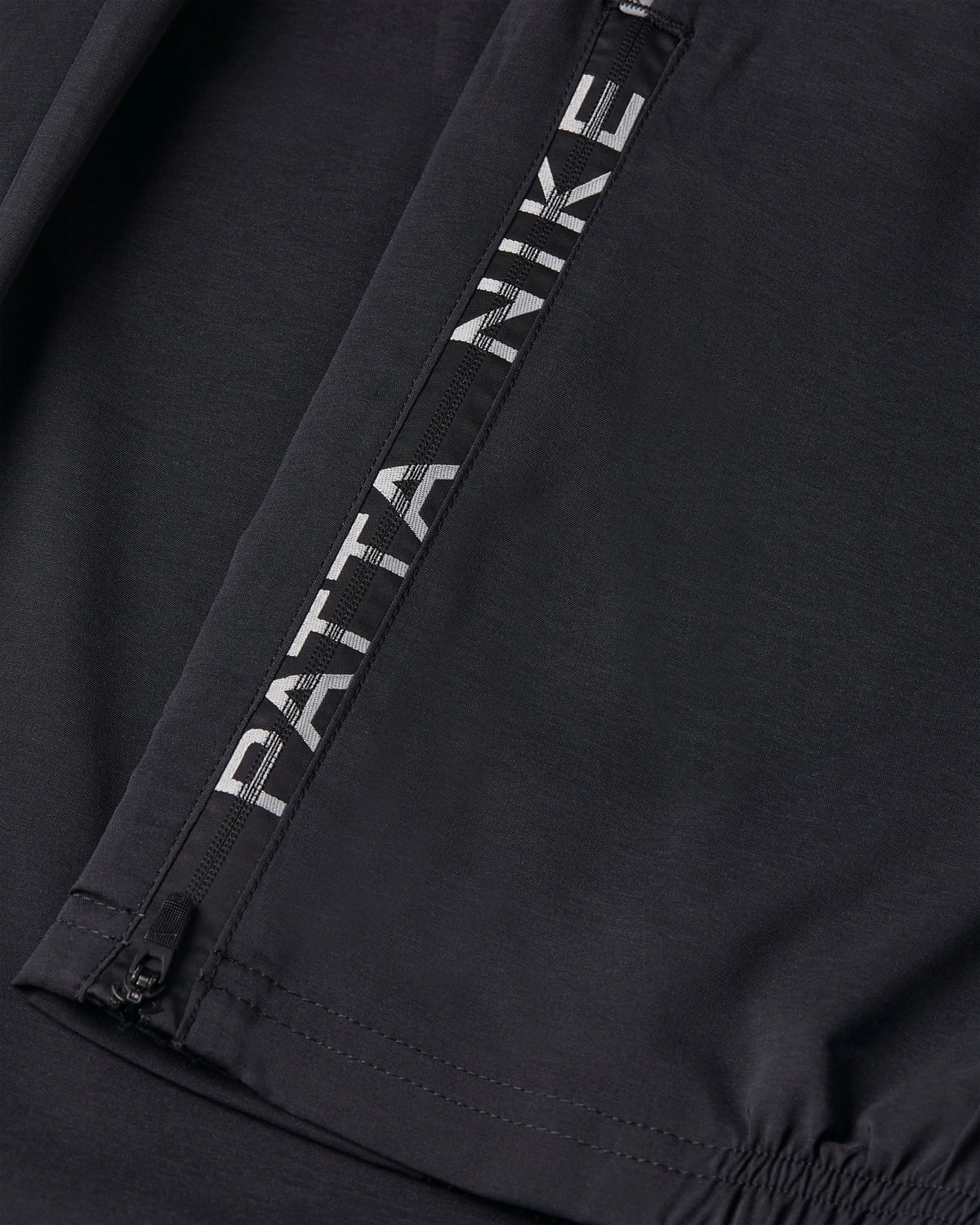 Close-up of the zippered ankle cuff with Patta Nike logo tape on black Nike x Patta Running Team track pants.