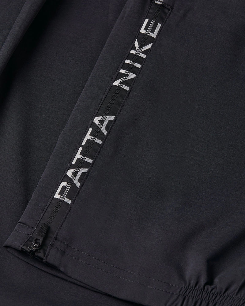 Close-up of the zippered ankle cuff with Patta Nike logo tape on black Nike x Patta Running Team track pants.
