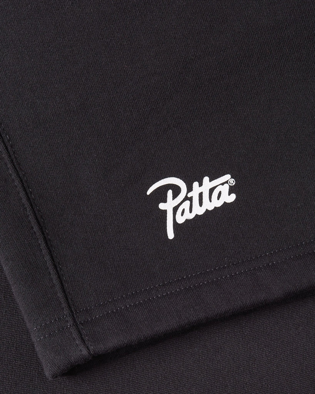 Close-up of the white Patta script logo printed on black Classic Jogging Shorts.