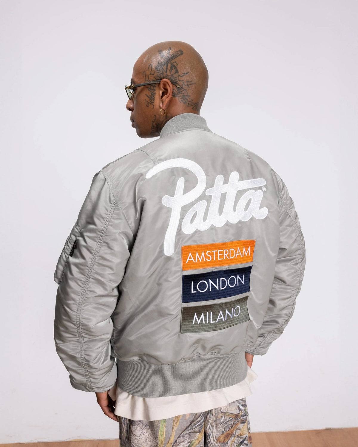 Back view of the silver Patta x Alpha Industries MA-1 bomber jacket featuring embroidered logo and city patches.