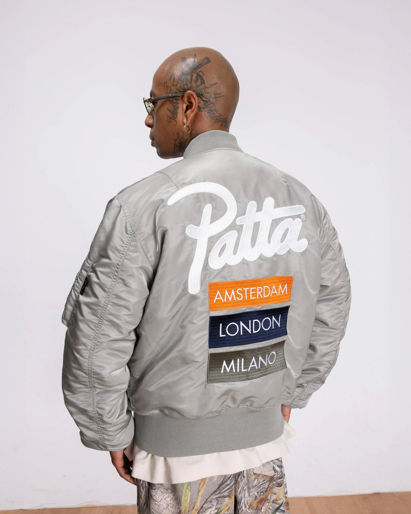 Back view of the silver Patta x Alpha Industries MA-1 bomber jacket featuring embroidered logo and city patches.