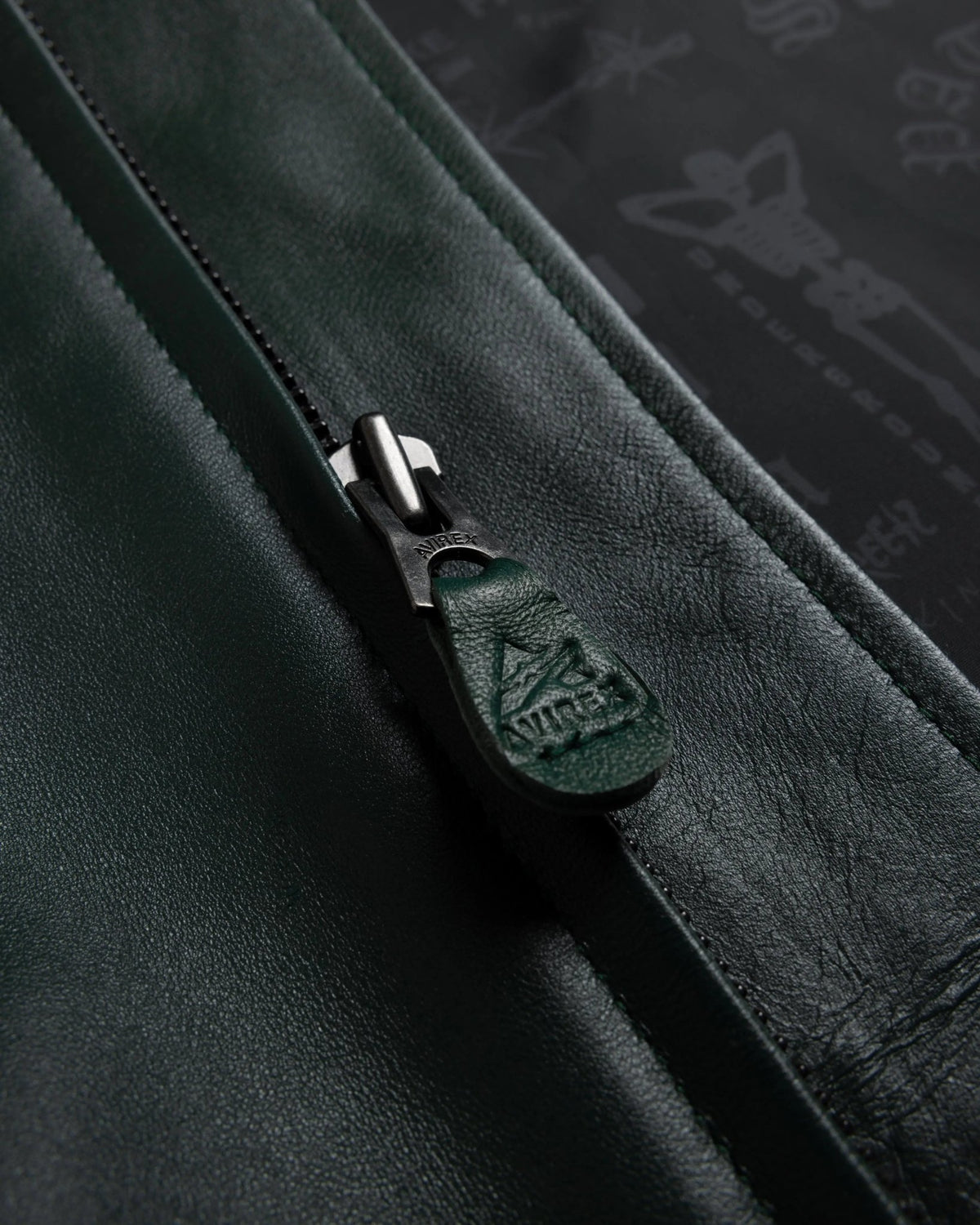 Close-up of the green leather zipper pull with embossed Avirex logo on the Patta x Avirex Icon Jacket.