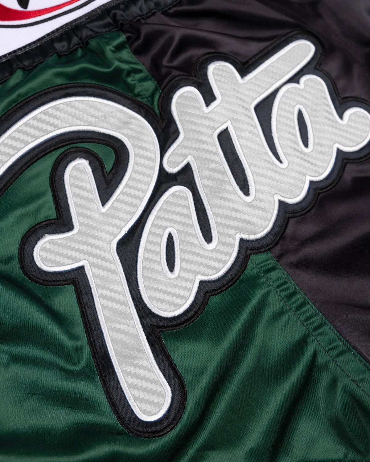Close-up of the white Patta script patch on green and black satin Muay Thai shorts.