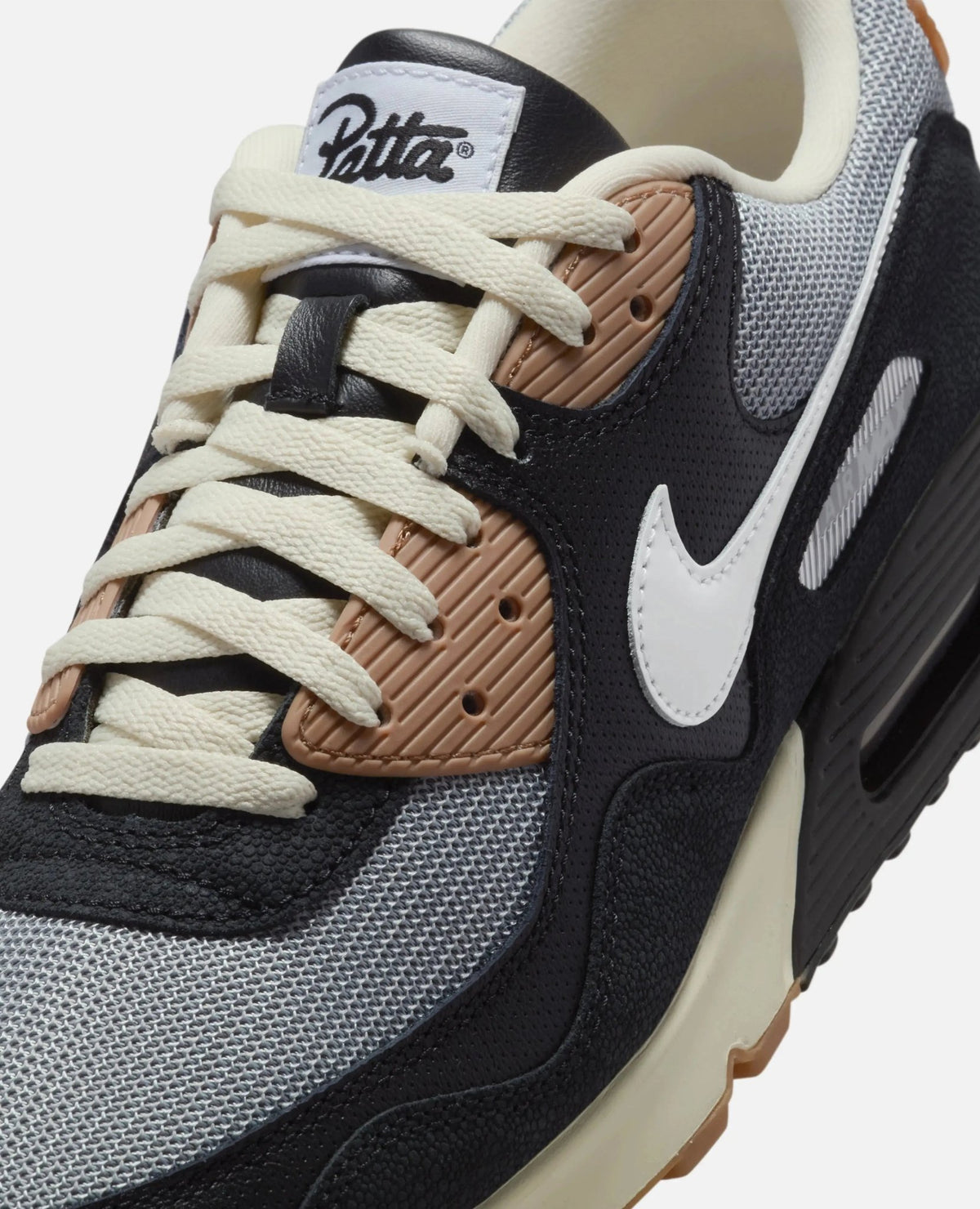 Close-up of Patta x Nike Air Max 90 SP sneaker showing tongue branding, mesh upper, laces, and Swoosh.