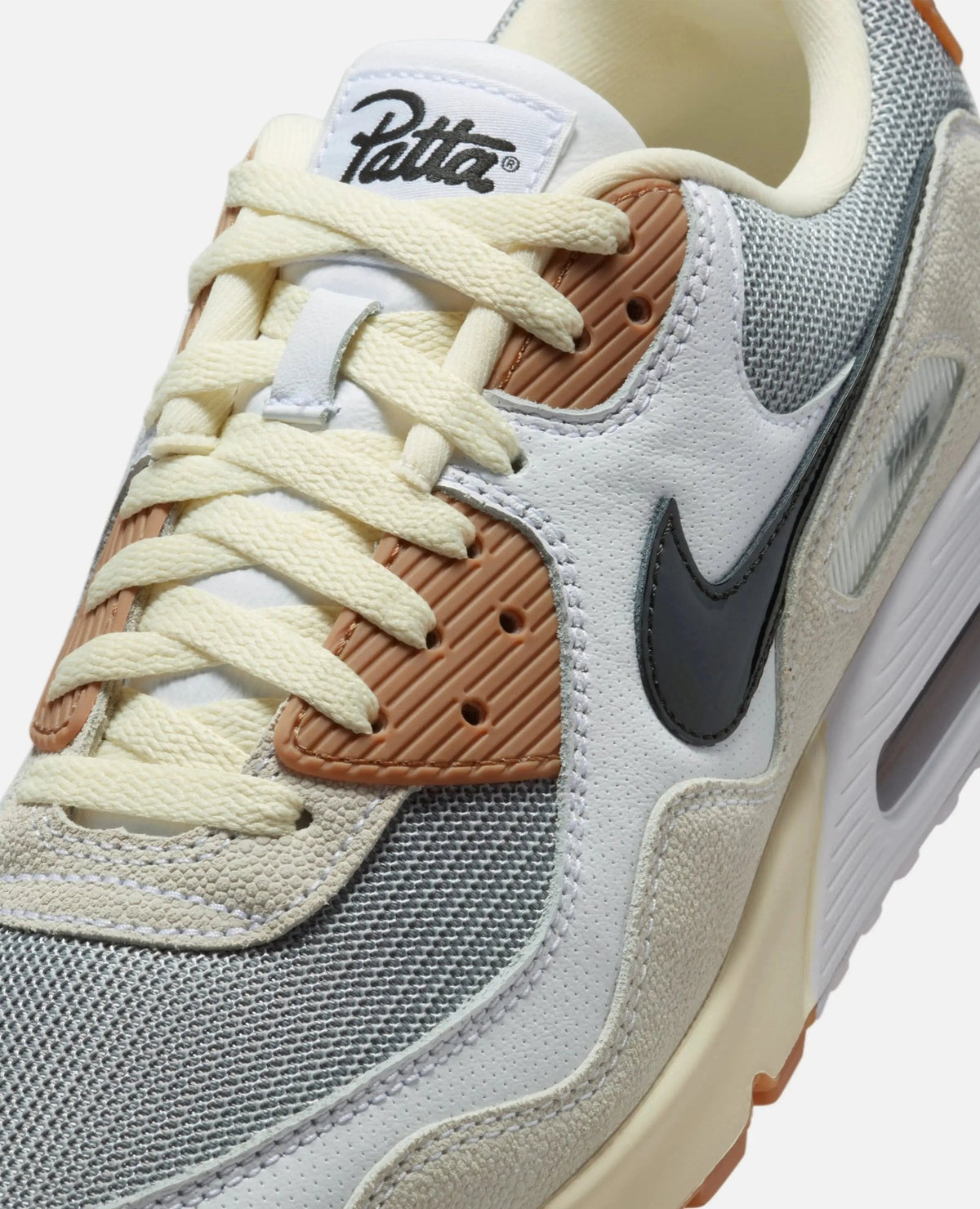Close-up of Patta x Nike Air Max 90 SP sneaker showing grey mesh, cream laces, and Patta tongue tag.