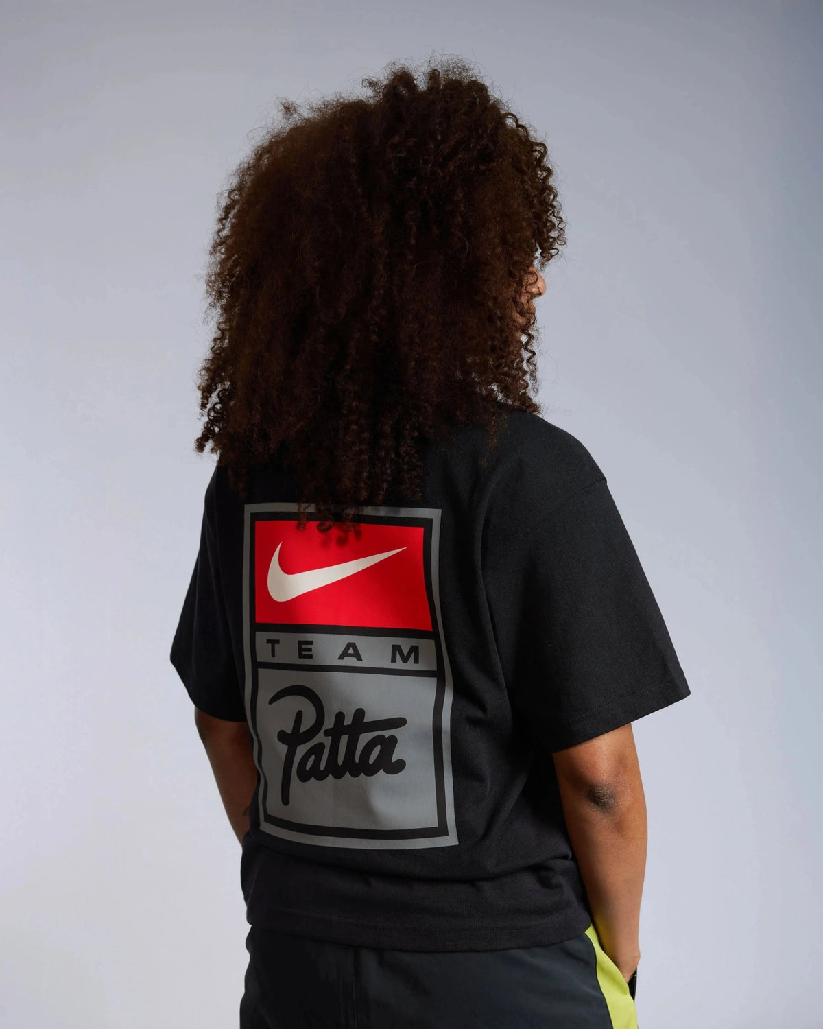 Model wearing the black Patta x Nike NRG T-shirt with a large Team Patta logo badge printed on the back.