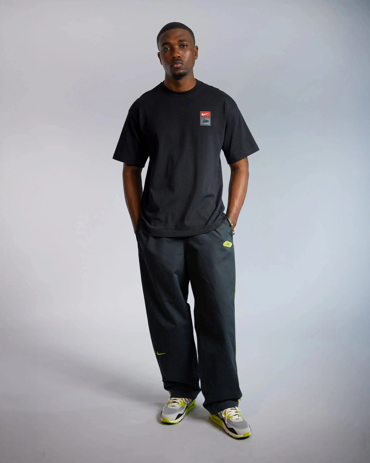 Male model wearing the black Patta x Nike NRG cotton T-shirt with chest badge in a studio setting.