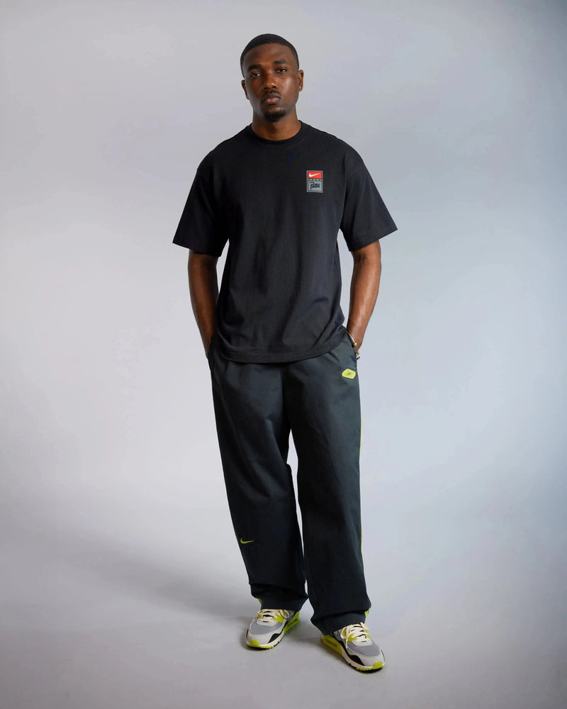 Male model wearing the black Patta x Nike NRG cotton T-shirt with chest badge in a studio setting.