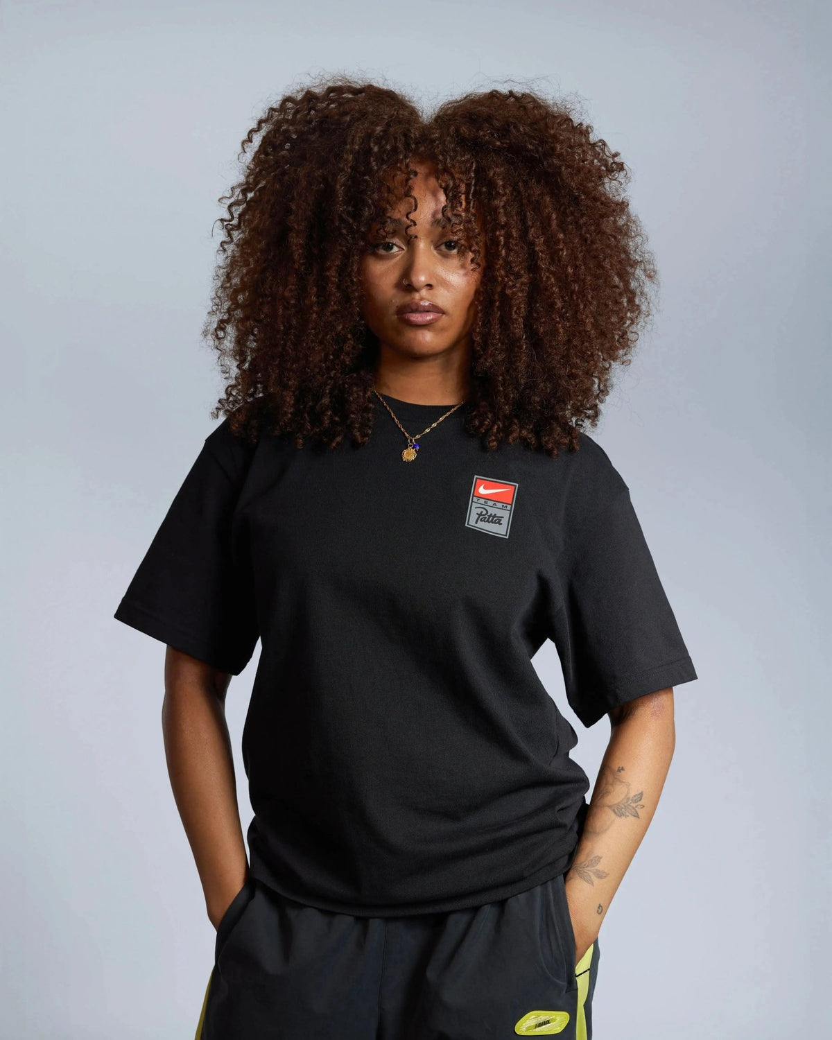 Model wearing the Patta x Nike NRG black graphic t-shirt with chest logo badge.