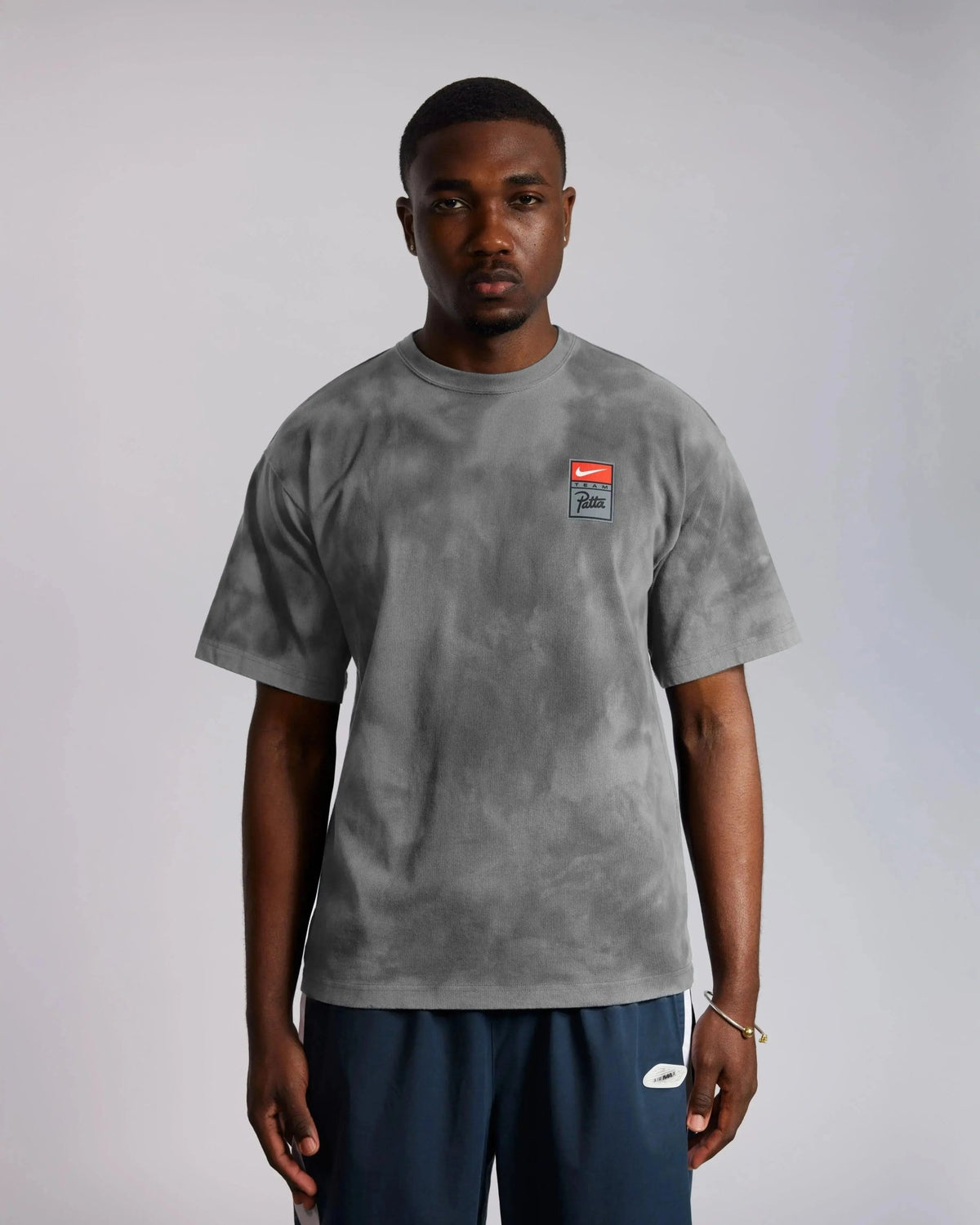 Model wearing the washed grey Patta x Nike NRG tie-dye t-shirt with chest logo badge.