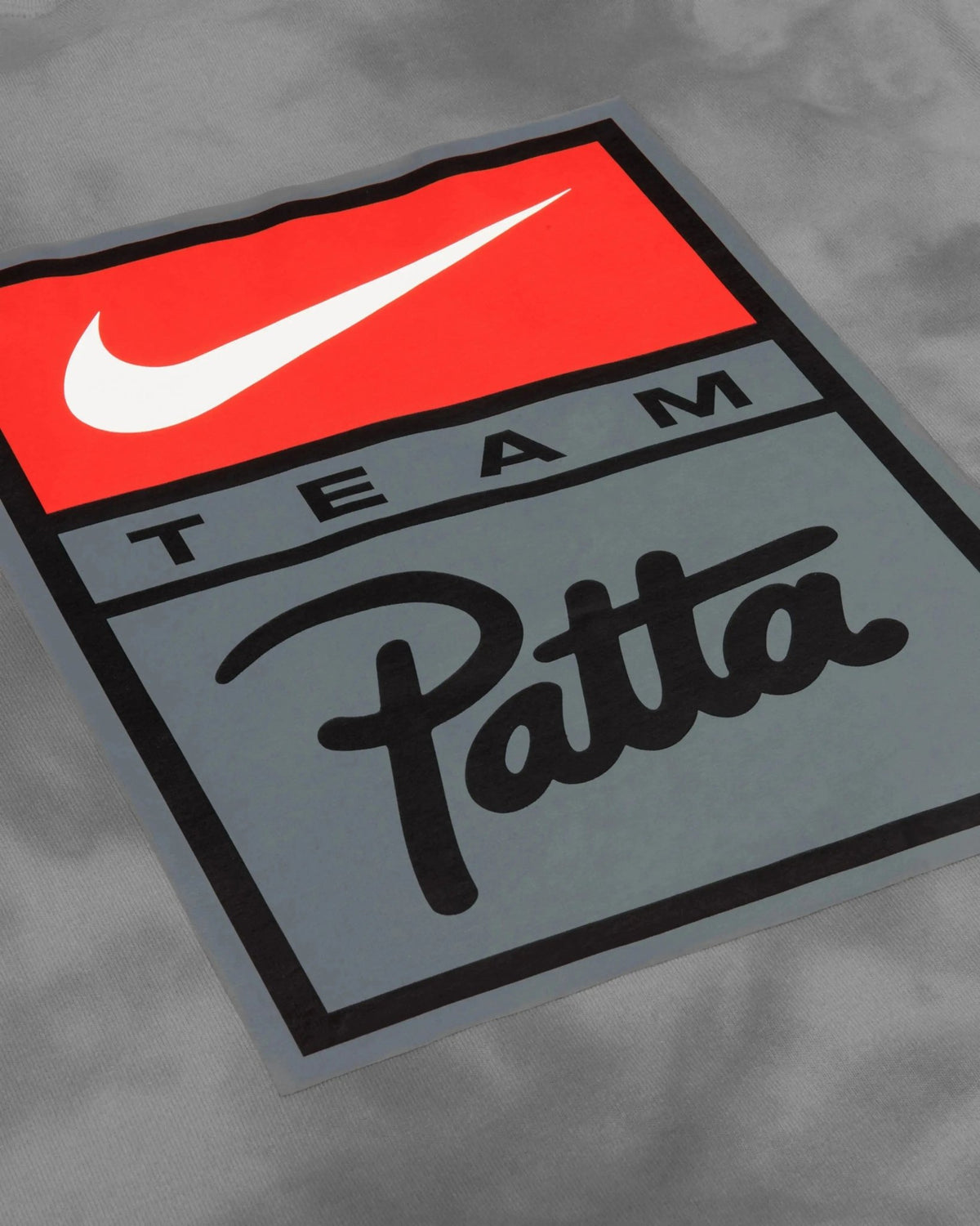 Close-up of the red and grey Team Patta and Nike Swoosh badge on a washed grey cotton T-shirt.