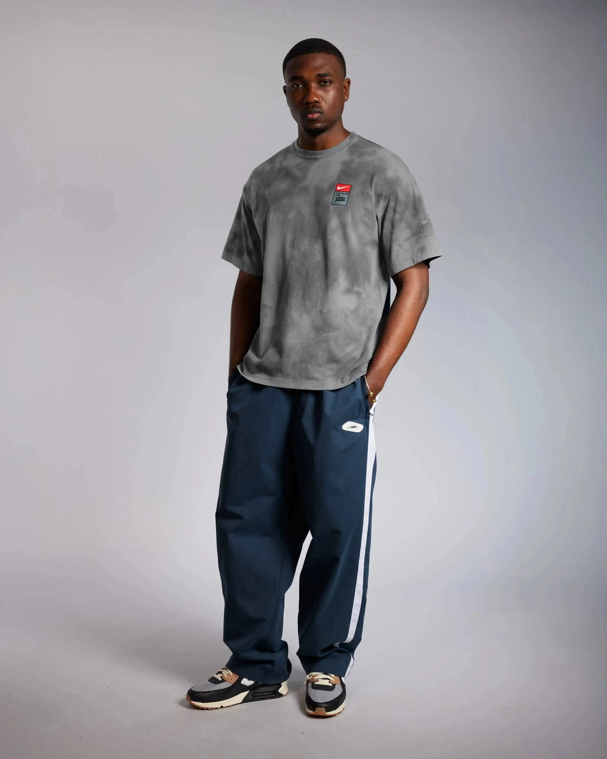 Male model wearing the washed grey Patta x Nike NRG T-shirt with navy track pants.