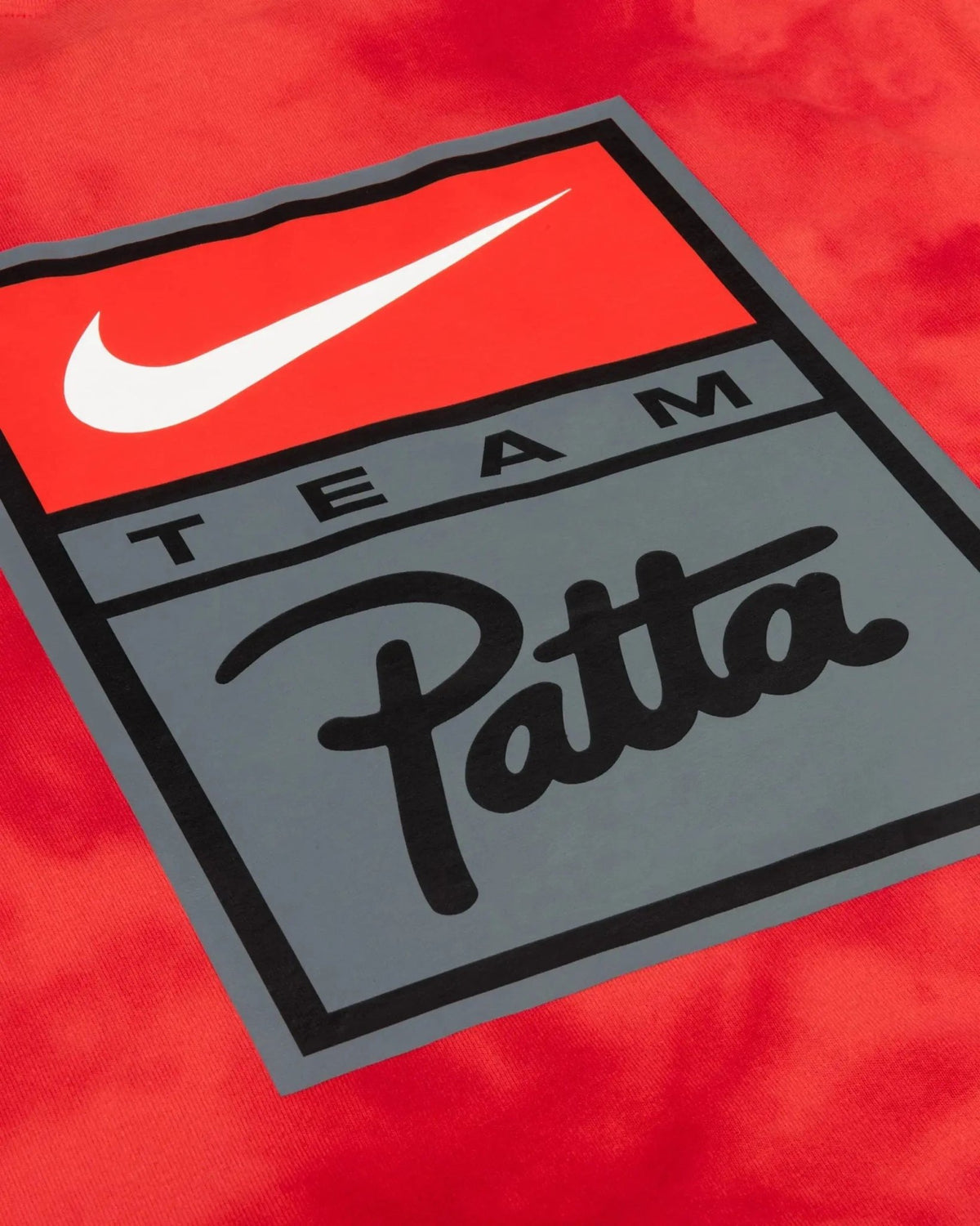 Close-up of the Nike Swoosh and Team Patta graphic badge printed on a red washed cotton T-shirt.