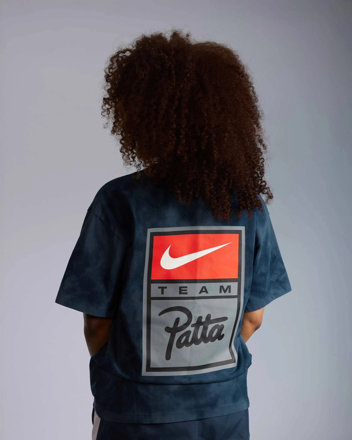 Back view of model wearing the washed dark blue Patta x Nike NRG T-shirt with a large team logo badge.