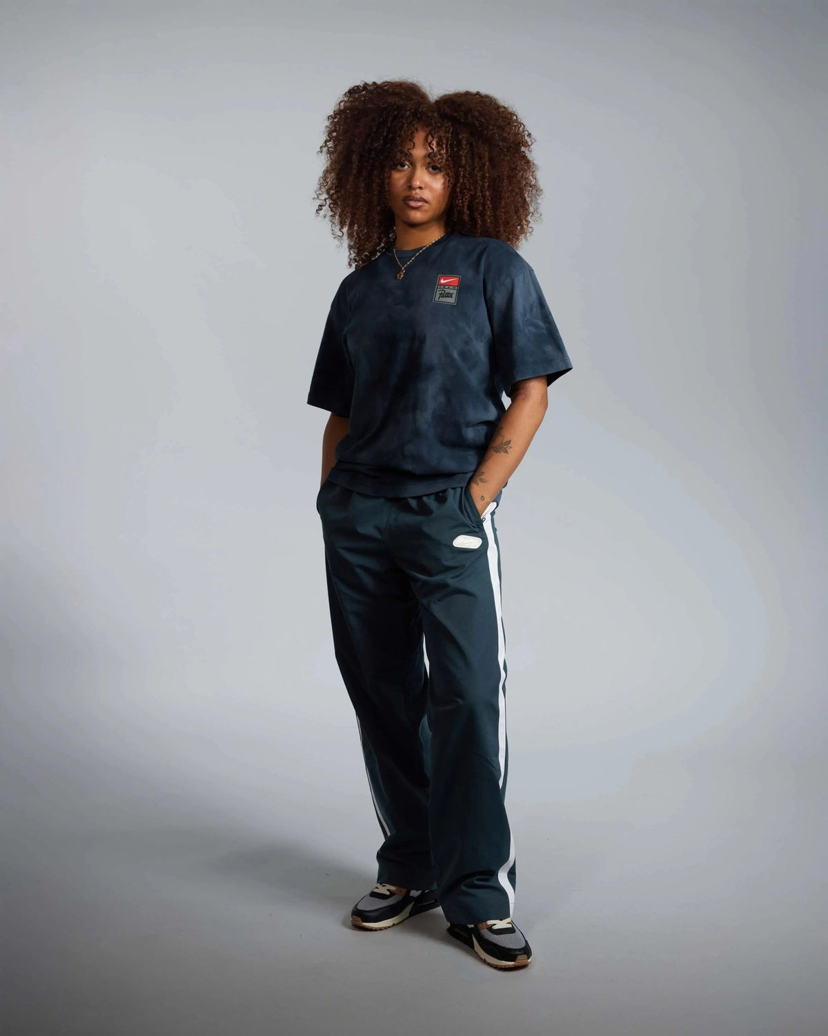 Female model wearing the dark blue washed Patta x Nike NRG T-shirt paired with matching track pants.
