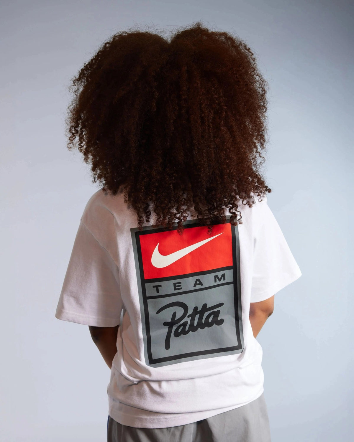 Back view of a model wearing the white Patta x Nike NRG T-shirt with a large graphic badge print.