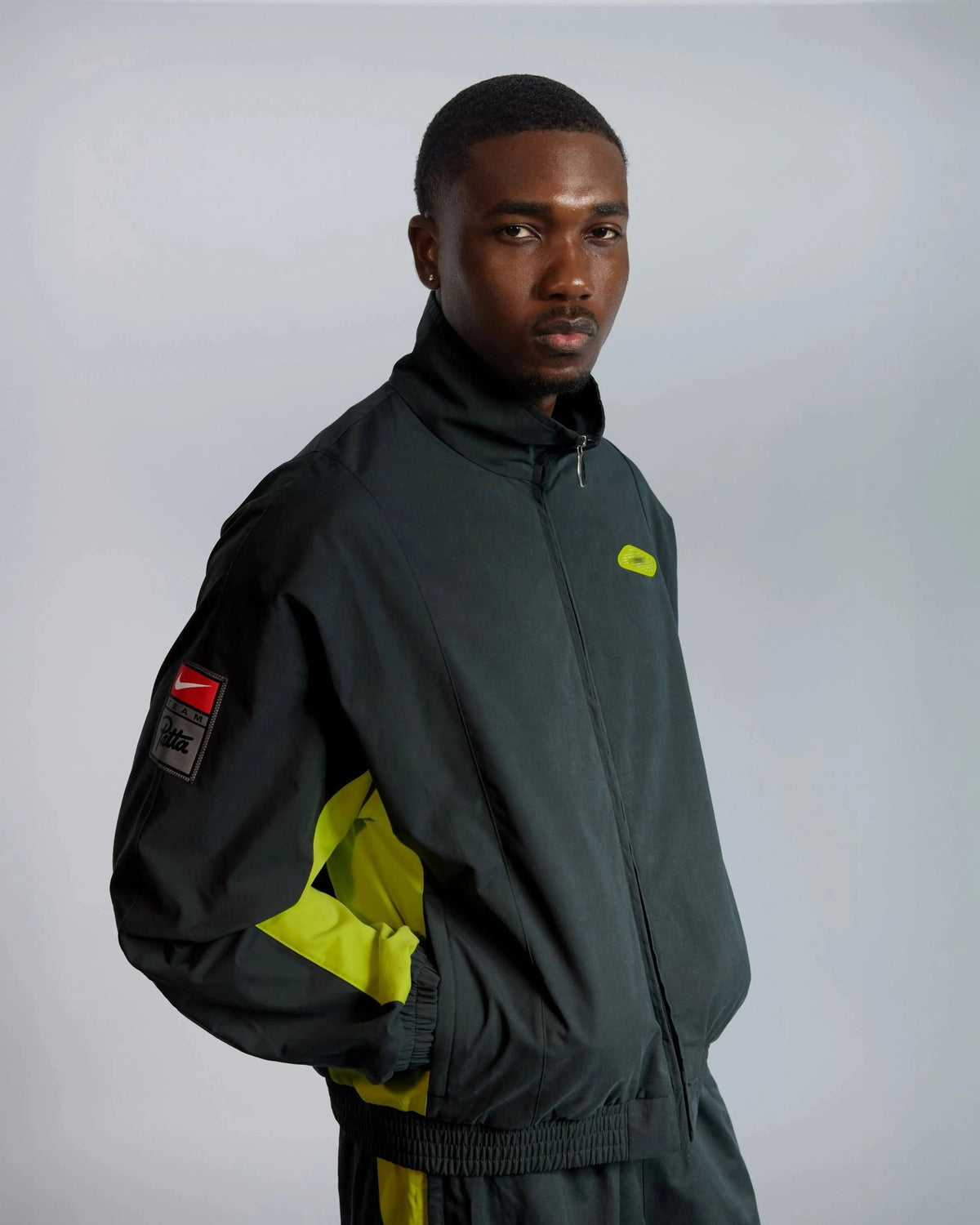Patta x Nike NRG Track Jacket in black and cyber worn by a male model in studio.