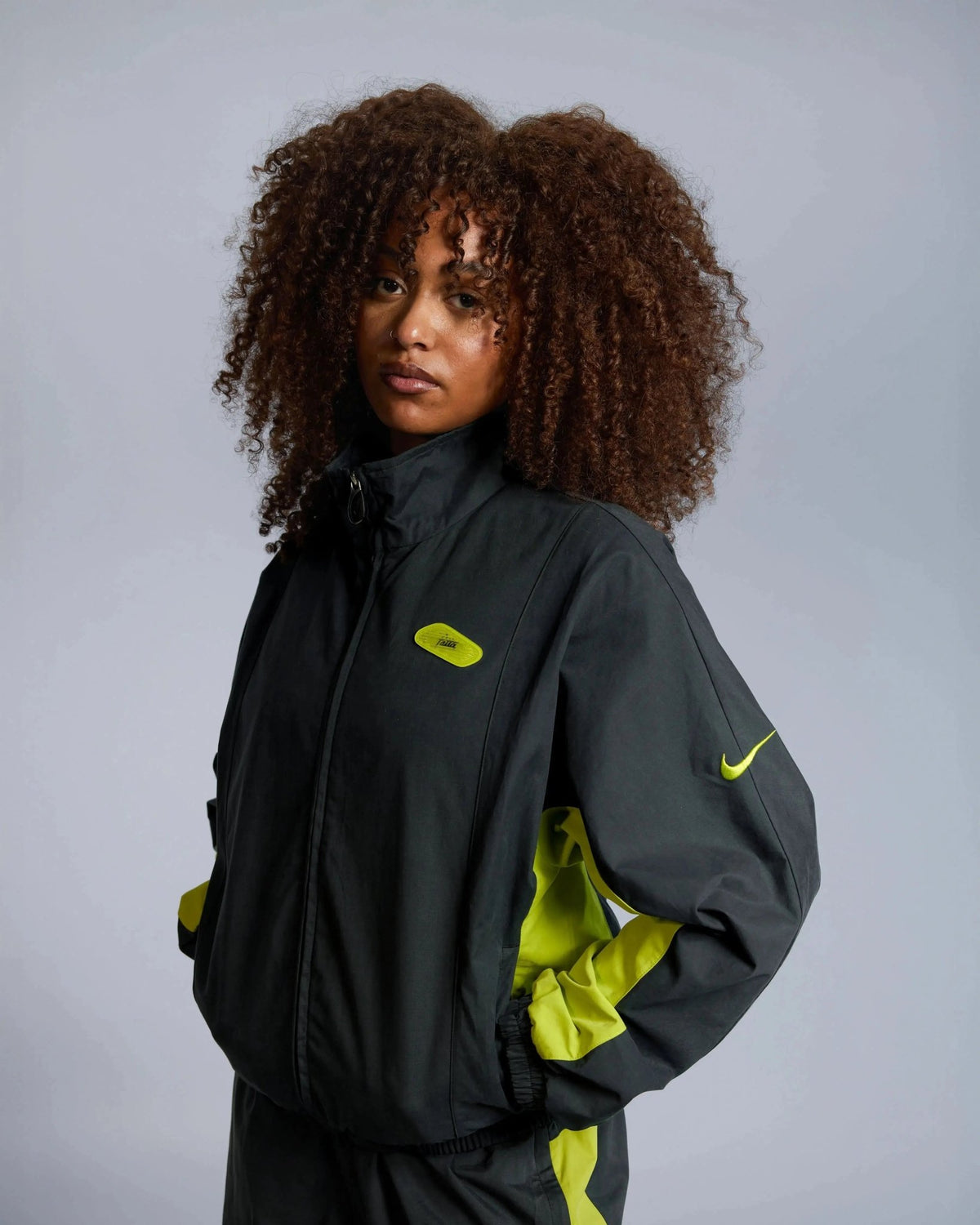 Model wearing the Patta x Nike NRG Track Jacket in black with vibrant cyber yellow panels and logos.