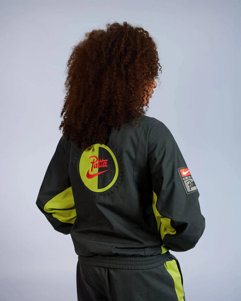 Back view of model wearing the Patta x Nike NRG Track Jacket in black and cyber with back logo patch.