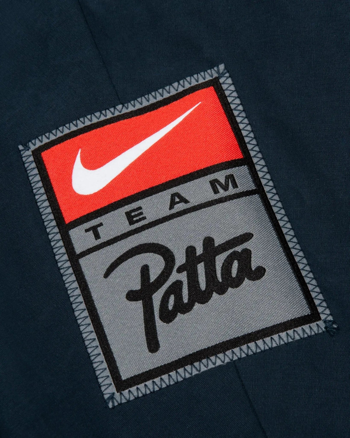 Close-up of the Nike and Team Patta logo patch on the deep ocean blue NRG Track Jacket.