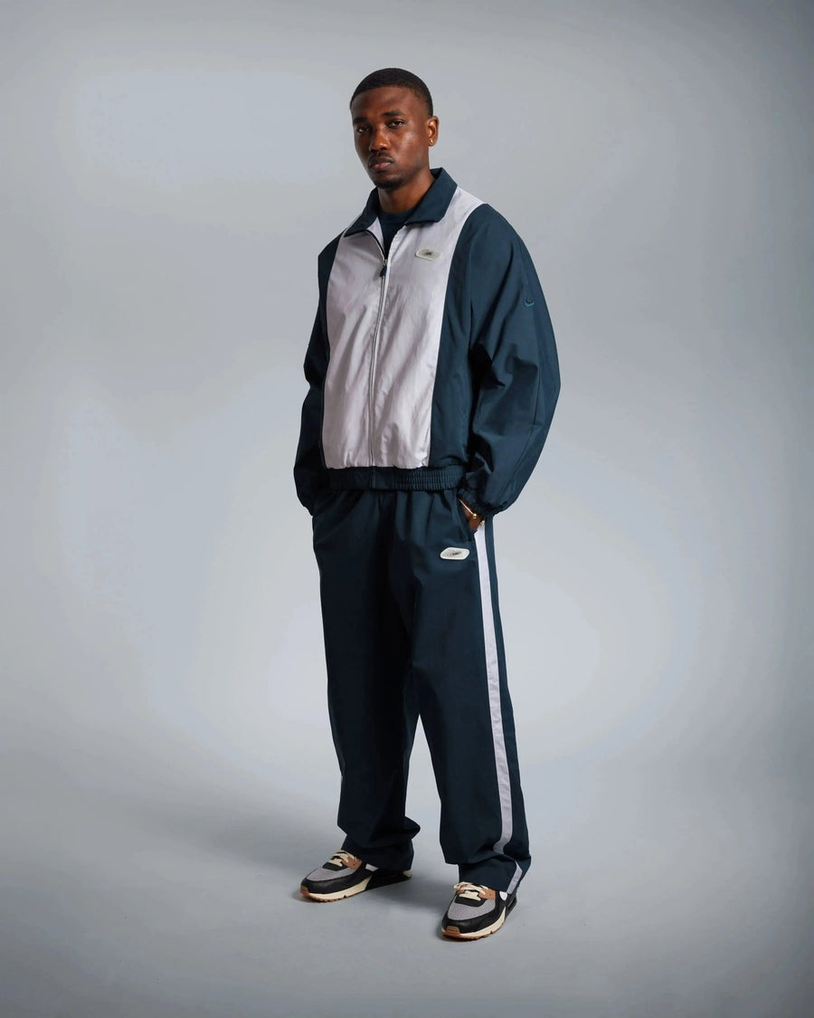 Model wearing the Patta x Nike NRG track jacket in deep ocean and white paired with matching pants.