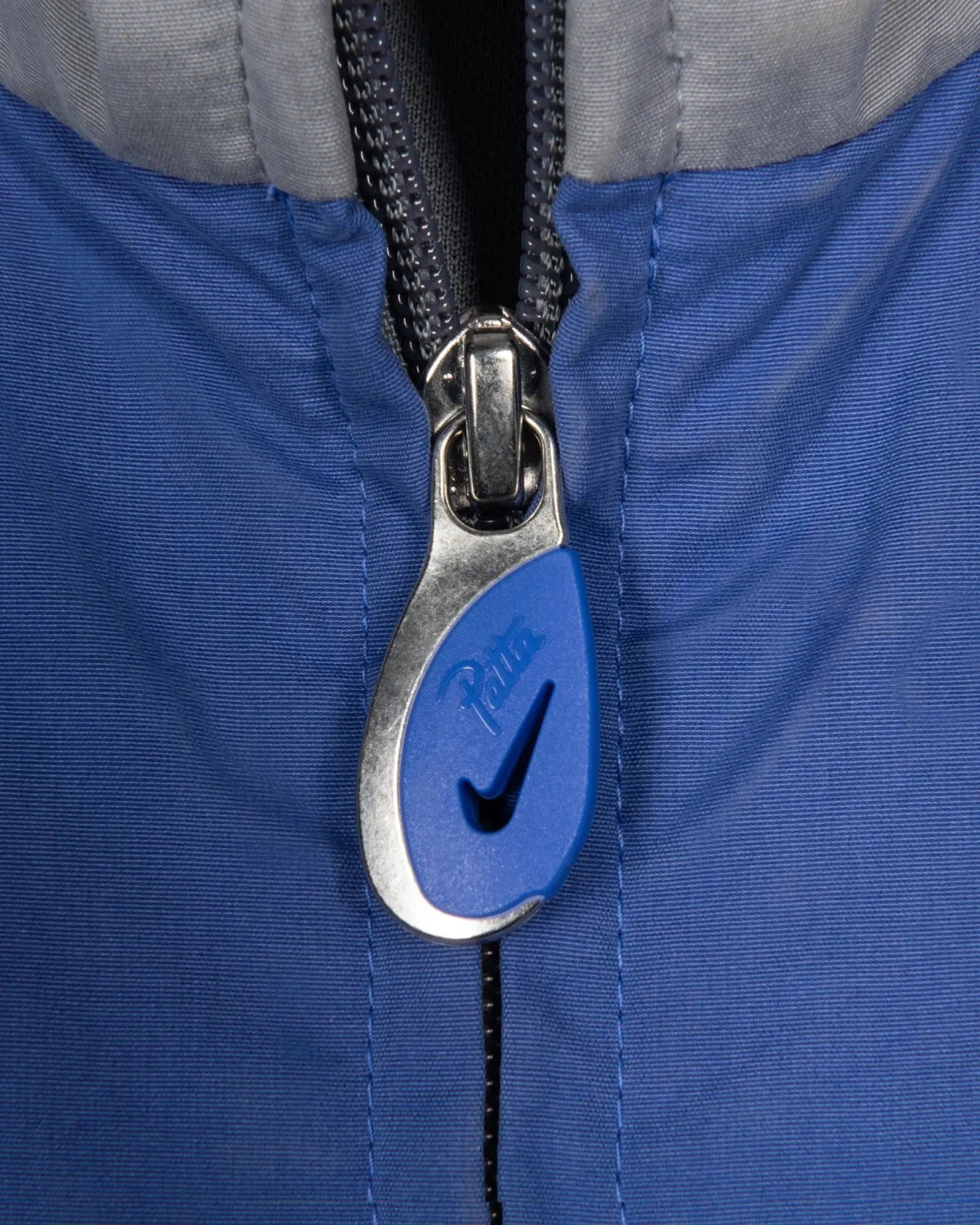 Close-up of the blue and silver custom zipper puller on the Patta x Nike NRG Track Jacket.