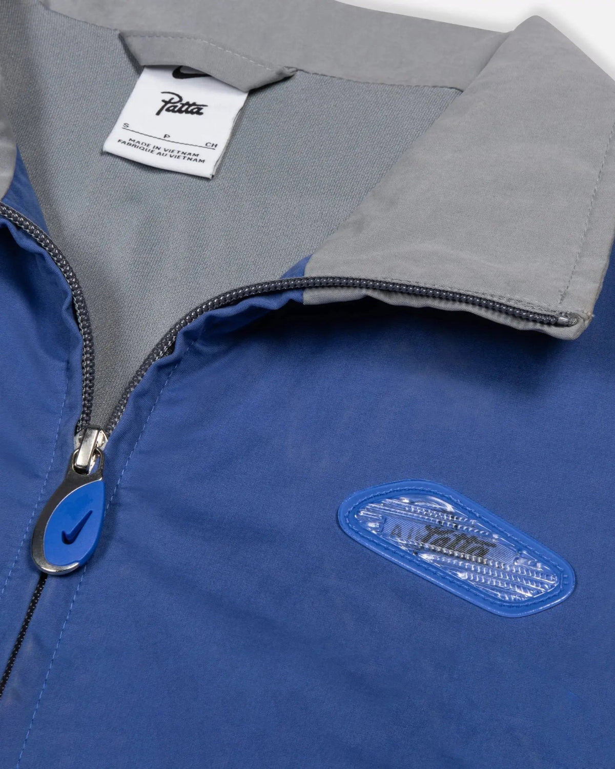 Collar and chest detail of the Patta x Nike NRG Track Jacket in sapphire blue with lenticular badge and zip puller.
