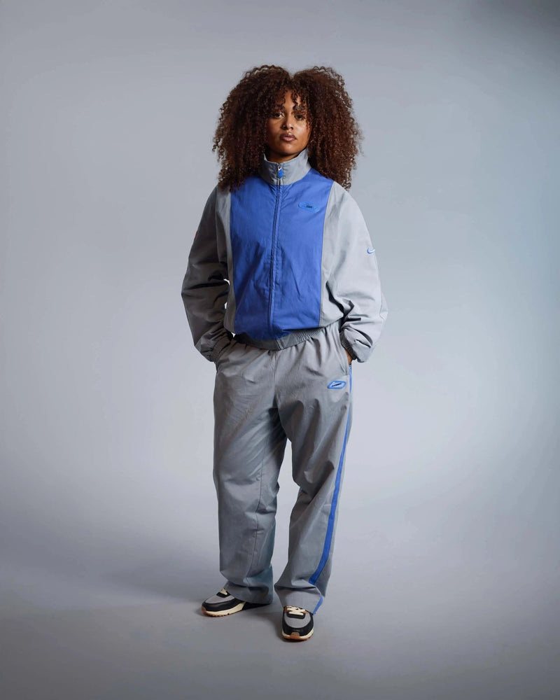 Patta x Nike NRG Track Jacket in Particle Grey and Sapphire worn by a model in a full-length studio shot.