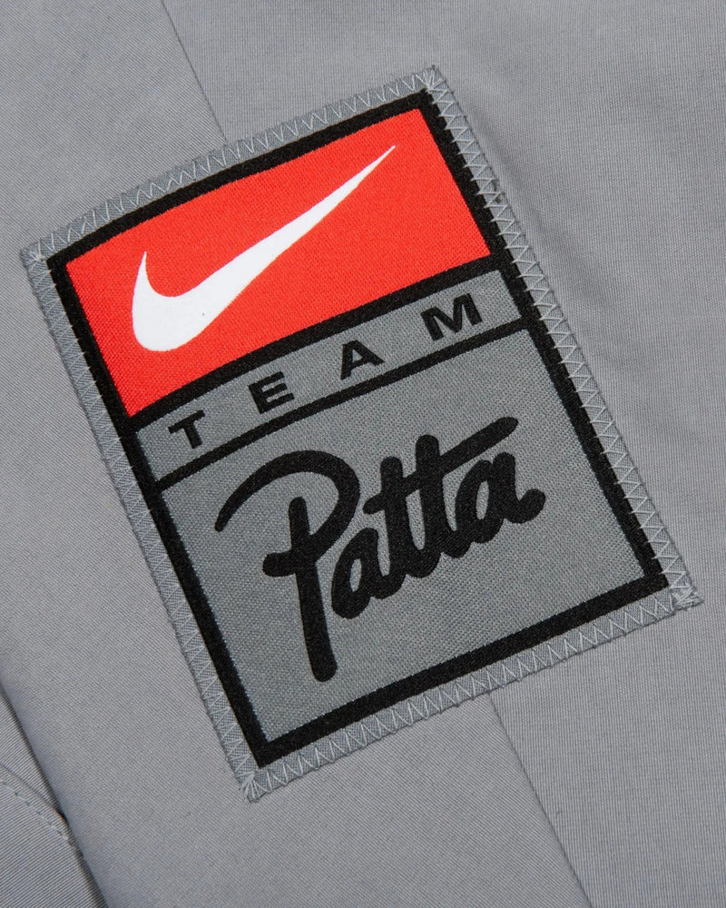 Close-up of the stitched Team Patta and Nike swoosh logo patch on the grey NRG track jacket.