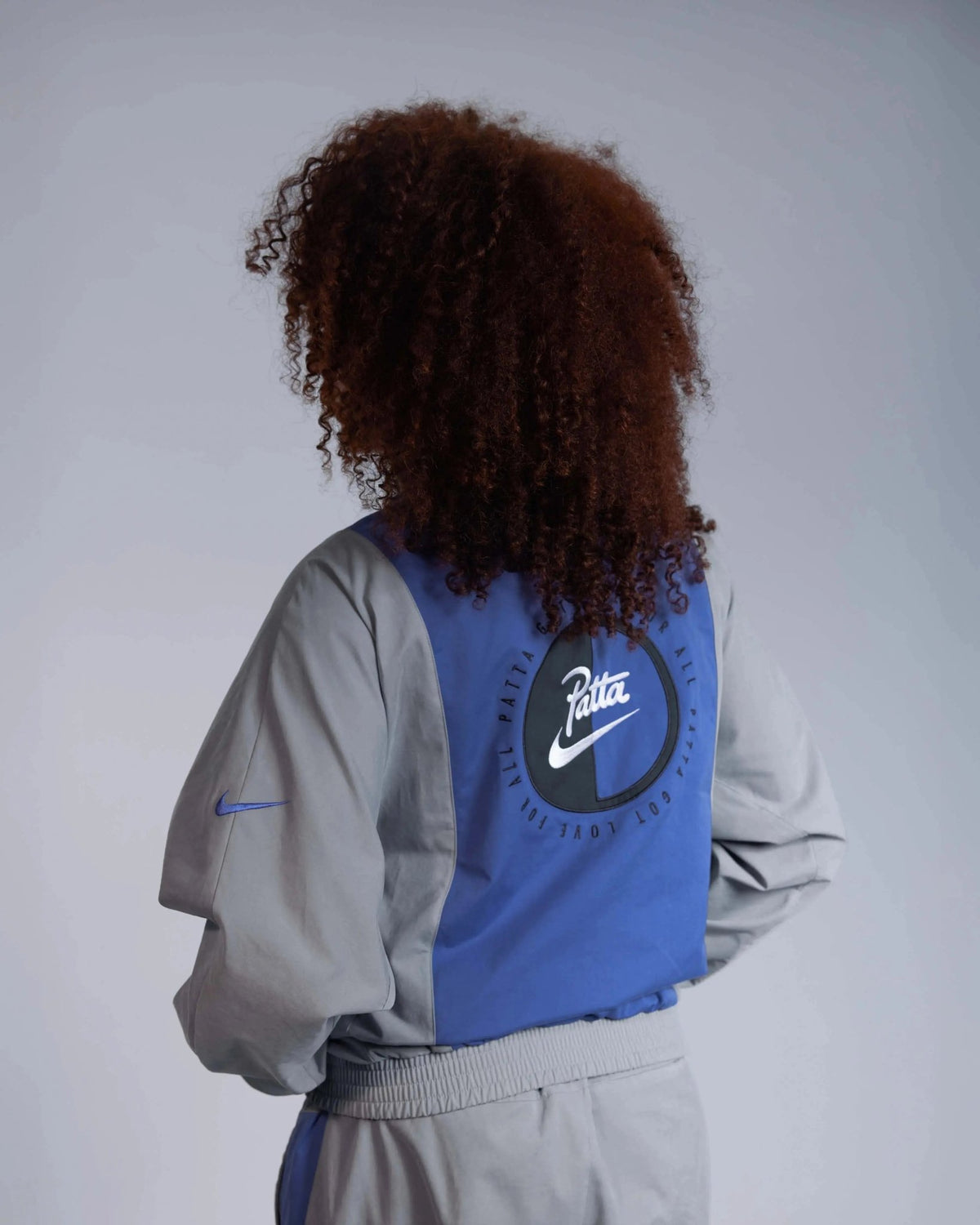 Back view of model wearing the Patta x Nike NRG Track Jacket in Particle Grey and Sapphire blue.