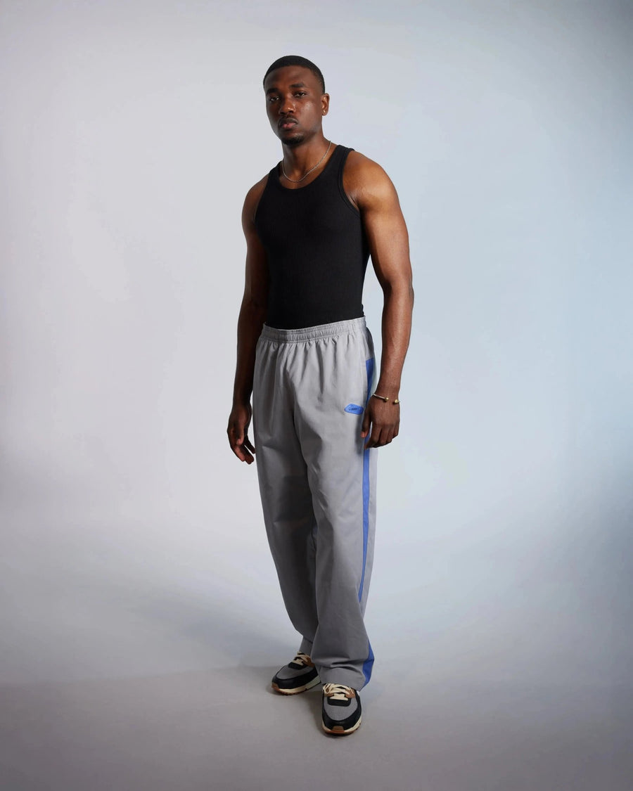 Male model wearing Patta x Nike NRG track pants in particle grey with sapphire blue stripes.