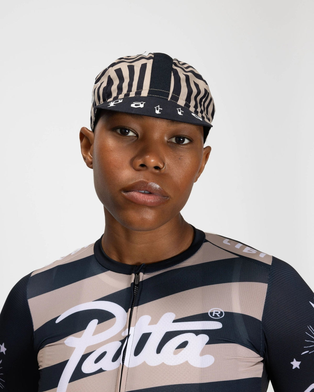 Model wearing the Patta x Rapha Cap II in black and stone stripe pattern with matching cycling jersey.