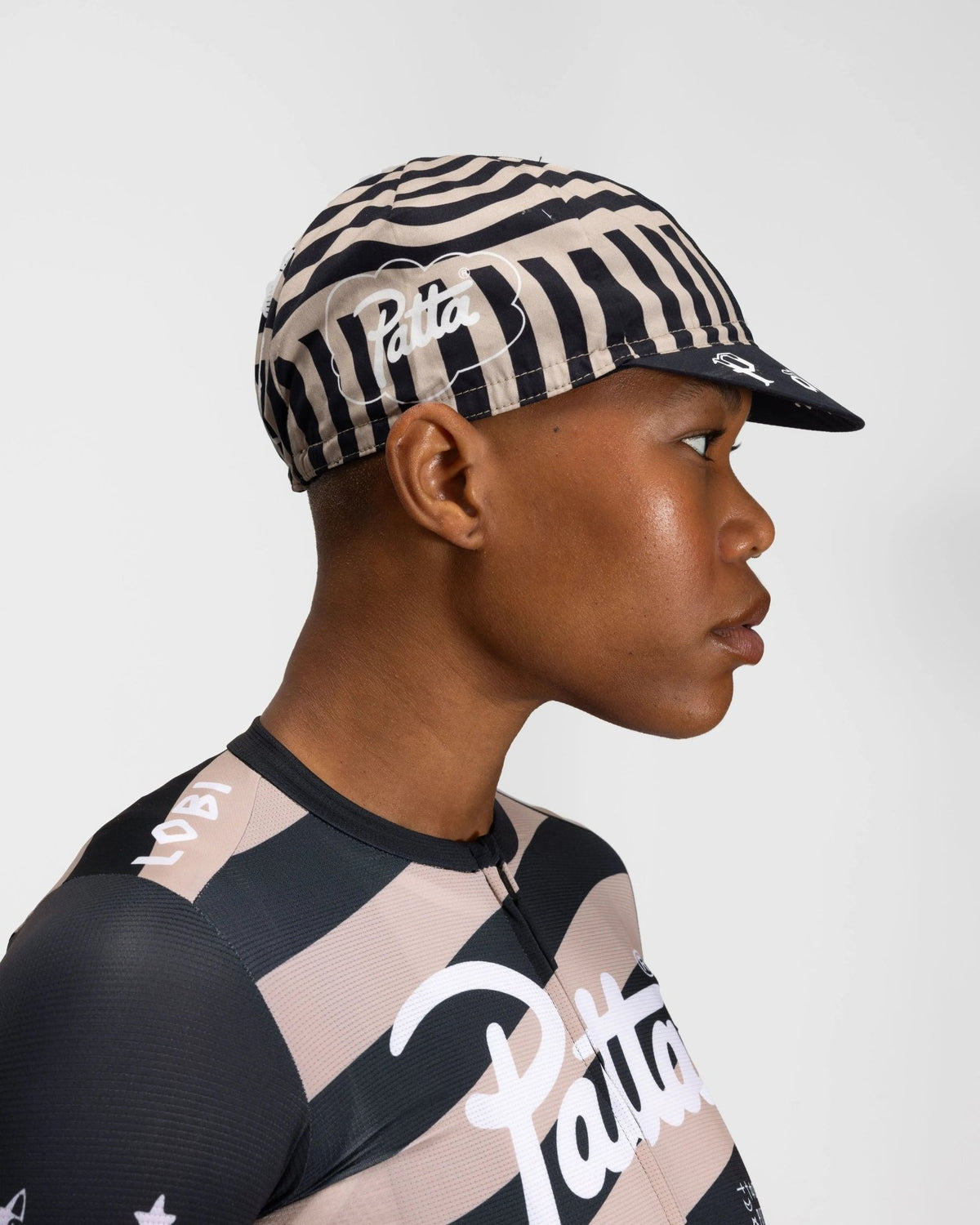 Side profile of a model wearing the striped black and stone Patta x Rapha Cap II cycling cap.