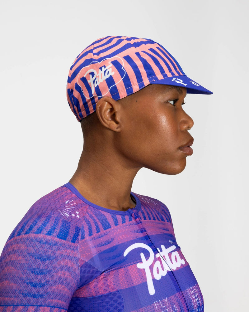 Side profile of a model wearing the Patta x Rapha Cap II in Flamingo Pink and Royal Blue.