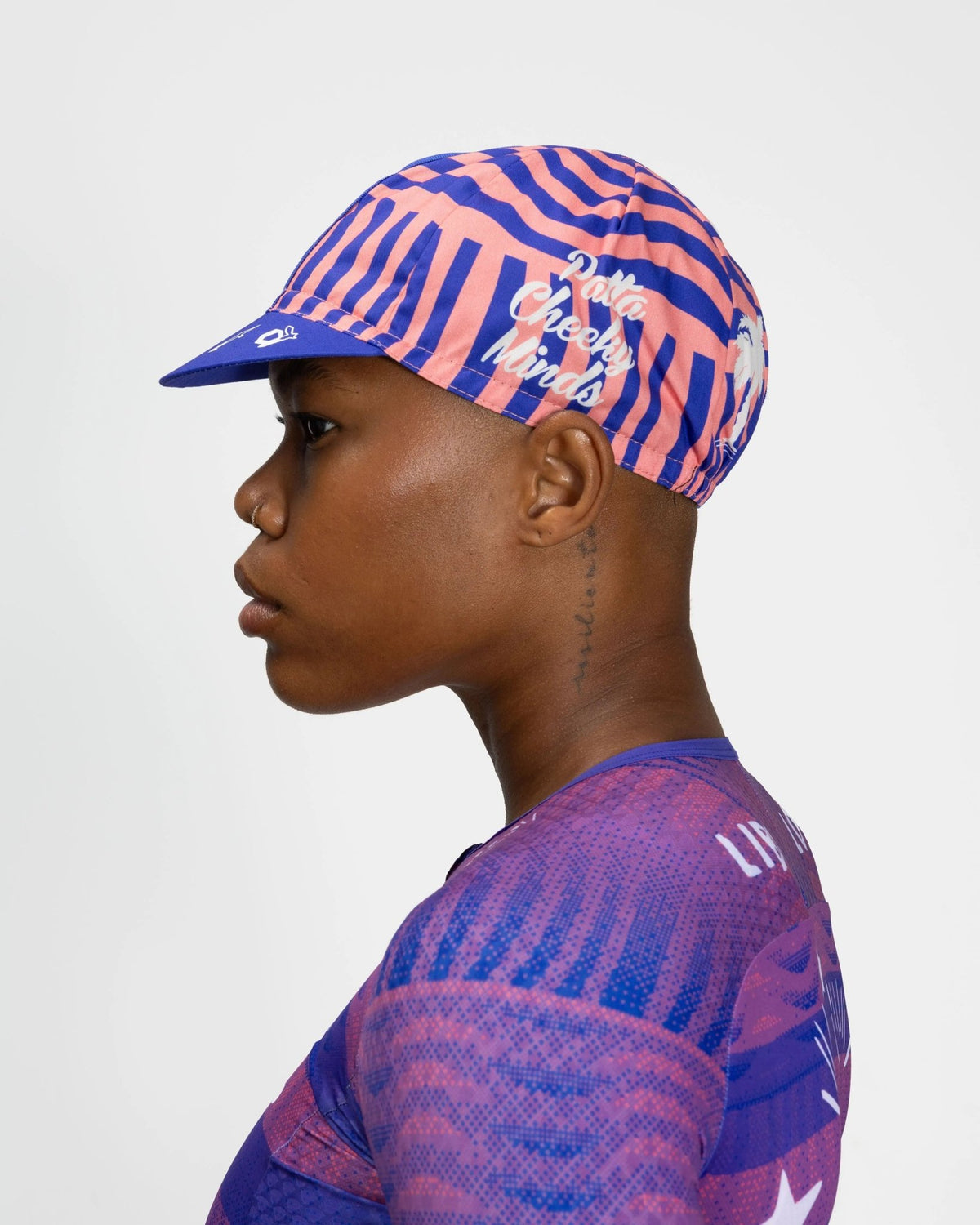 Side view of model wearing the flamingo pink and royal blue striped Patta x Rapha Cap II.