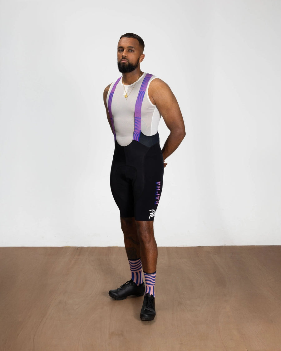 Model wearing black Patta x Rapha cycling bib shorts with pink and royal blue straps.