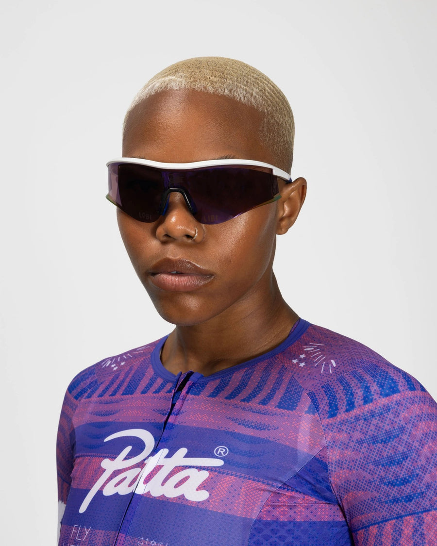 Model wearing white Patta x Rapha Reis sunglasses with dark cycling shield lenses.