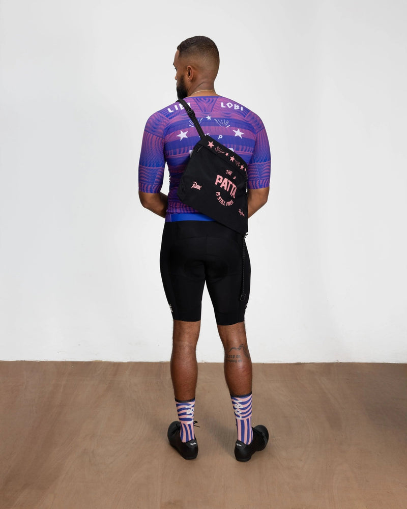 Patta x Rapha Tech Musette bag in black with pink graphics worn across a model's back.